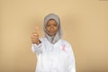 Muslim female doctor in headscarf and white coat wears pink breast cancer awareness ribbon raising thumb up