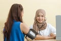 Muslim female doctor using sphygmomanometer with stethoscope checking blood pressure to patient in the hospital Royalty Free Stock Photo