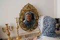 Muslim girl with covered head in a blue scarf laughs and smiles and looks in the mirror