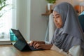 Muslim girl doing homework and using tablet with tutor via the internet on a table at night. Concept of online learning at home