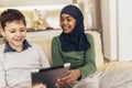 Muslim girl and her caucasina friend sitting at home using digital tablet