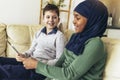 Muslim girl and her caucasina friend sitting on sofa at home using digital tablet