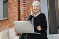 Muslim girl in hijab wearing wireless headphones, listening favorite songs online working on laptop Royalty Free Stock Photo