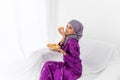 Muslim girl wearing hijab celebrates end of Ramadan, in purple kebaya dress, and holding food Royalty Free Stock Photo