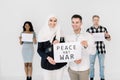 Muslim girl in white hijab and Caucasian man smiling while holding a poster with an inscription PEACE NO WAR Royalty Free Stock Photo