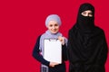 Muslim girls on a red background. A young girl holds a folder, white sheet, smiles and looks at the camera, another Royalty Free Stock Photo