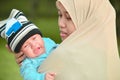 Muslim hijabi mother calming his crying infant baby in her arm at outdoor park in sunny day Royalty Free Stock Photo