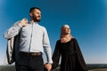 Muslim love story on the blue sky background. cheerful mixed couple smiles and hugs . Woman weared in hijab looks to her