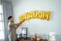 muslim male decorating the wall with ramadan balloon text