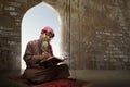 Muslim man with a beard wearing keffiyeh with agal sitting and reading the Quran on the prayer rug