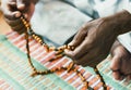 Muslim man wearing a light green djellaba and handling a rosary while sitting on a multicolored prayer mat