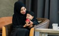Muslim mother wearing traditional black dress and headscarf, carrying little baby boy, smiling with happiness, feeding red apple, Royalty Free Stock Photo
