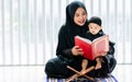 Muslim mother wearing traditional black dress and headscarf, carrying little baby boy, smiling, reading scripture, holding prayer Royalty Free Stock Photo