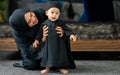 Muslim mother wearing traditional black dress and headscarf, carrying little boy, smiling with happiness, teaching baby to learn Royalty Free Stock Photo