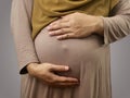 Muslim pregnant mother wearing hijab, anonymous mom holding her big belly