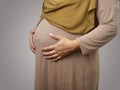 Muslim pregnant mother wearing hijab, anonymous mom holding her big belly