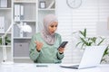 Surprised muslim businesswoman reacting to mobile phone content in office Royalty Free Stock Photo