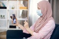 Muslim sick woman in hijab and protective mask, holding cell phone in one hand and pills in another one. African woman