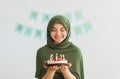 Muslim teen girl in hijab holding birthday cake with burning candles, celebrating b-day at home Royalty Free Stock Photo