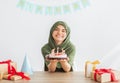 Muslim teen girl in hijab holding delicious birthday cake at table with gift boxes, celebrating festive occasion at home Royalty Free Stock Photo