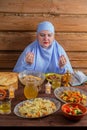 A Muslim woman in a blue hijab at the Ramadan iftar table says bismi llah raising her hands Royalty Free Stock Photo