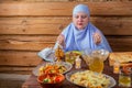 A Muslim woman in a blue hijab at the table begins a meal, the holiday of Eid al-Fitr says bismi llah, raising her hands Royalty Free Stock Photo