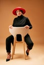 Muslim woman, chair and fashion, beauty and hat with trendy outfit, focus attitude and studio background. Mature