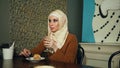 Muslim woman in hijab eats dessert in cafe.