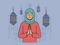 Muslim woman in hijab makes prayer gesture standing near mosque and traditional islamic lanterns