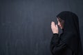 Muslim woman making traditional prayer to God in front of black chalkboard