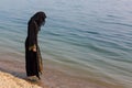 A Muslim woman in national clothes wets her feet in the sea Royalty Free Stock Photo