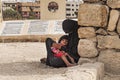 Muslim woman sits on the ground in Paris and holds a sleeping child in her arms