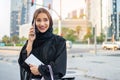 Muslim woman in traditional clothes holding shopping bags and wallet and talking on mobile phone on the street. Royalty Free Stock Photo