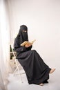 muslim woman wearing black hijab long dress is sitting reading al qur'an