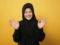 Muslim woman wearing hijab looking at camera smiling and waving her hands saying hi or goodbye farewell gesture against yellow Royalty Free Stock Photo