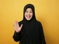 Muslim woman wearing hijab looking at camera smiling and waving her hands saying hi or goodbye farewell gesture against yellow Royalty Free Stock Photo