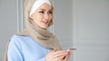 Muslim woman wearing hijab is speaking smartphone using wireless earphone. Royalty Free Stock Photo