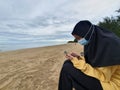 Muslim woman wearing protective mask using smart phone while sitting in the beach during covid 19 coronavirus pandemic Royalty Free Stock Photo