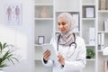Muslim woman in white medical coat standing inside medical office of clinic, female doctor using tablet computer Royalty Free Stock Photo