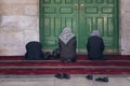 Muslim women praying for Allah god near the green door of a mosque. Three shoeless women sitting against the muslim shrine