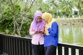 Muslimah enjoying outdoor, having discussion at park and one of them holding mobile phone