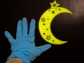 Human hand in blue rubber with yellow moon decoration for Ramadan kareem month at dark background