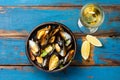 Mussels in clay bowl, glass of white wine and lemon