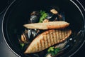 Mussels in a frying pan in tomato sauce and croutons on a stone plate.