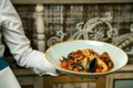 Mussels with tomato and olives - delicious and healthy dinner in a restaurant. A plate of seafood in male hands closeup waiter.