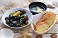 Mussels in wine-butter sauce, sprinkled with parsley, served with bread. Clams in a bowl, on white wood background.
