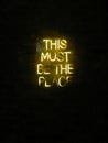 This Must Be The Place neon light sign on dark brick wall Royalty Free Stock Photo