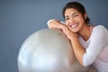 This is a must-have for every home gym. a sporty young woman leaning on a pilates ball against a grey background. Royalty Free Stock Photo