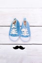 Mustache and blue children`s shoes stand on a white wooden backg