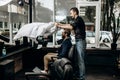 Mustachioed barber dressed in a black shirt puts a cape on the stylish man sitting in the armchair in a barbershop